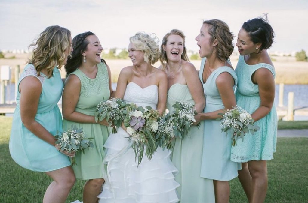 bride and bridesmaid bride has on a white dress and bridesmaid are clad in teal for an outer banks wedding with obx wedding flowers