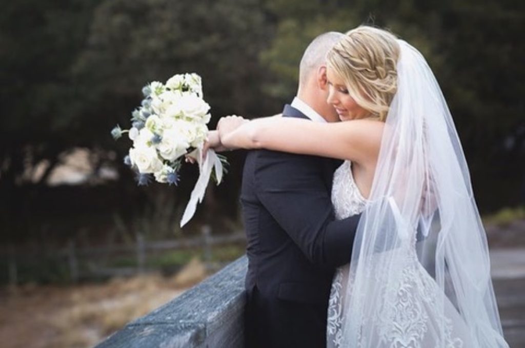 bride and groom embrace holding white bouquet of flowers designed by obx wedding flowers